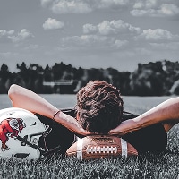 Senior photo of senior laying next to football helmet in field